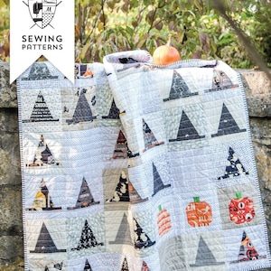 May include: A patchwork quilt featuring a repeating pattern of witch hats and pumpkins in various shades of black, white, gray, and orange. The quilt has a grid-like construction with visible stitching and a small orange pumpkin resting on top.