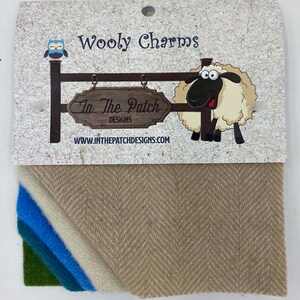 May include: A pack of four fabric squares in green, teal, blue, and white. The fabric is a herringbone weave. The pack is labeled "Wooly Charms" and "In The Patch Designs" with a cartoon sheep and owl.