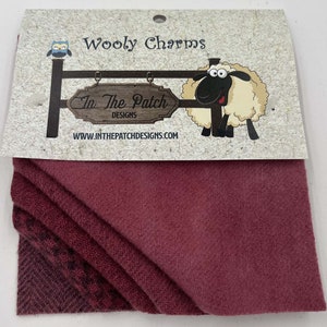 May include: A pack of four burgundy wool charm squares with the text "Wooly Charms" and "In The Patch Designs" on the packaging. The packaging also features a cartoon sheep.