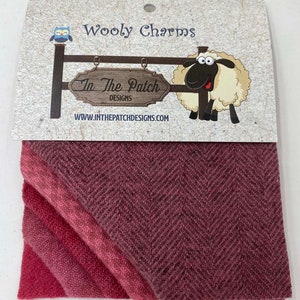 May include: Wooly Charms fabric in a pink and red ombre herringbone pattern. The fabric is folded in thirds and is packaged with a label that reads "Wooly Charms" and "In The Patch Designs" with a cartoon sheep and owl.