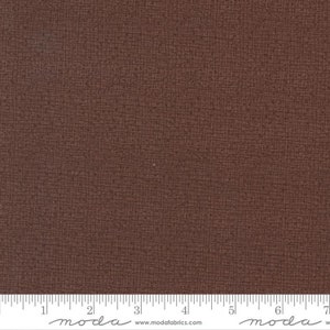 May include: A close-up of a brown fabric with a subtle textured pattern. The fabric is measured with a ruler in inches.