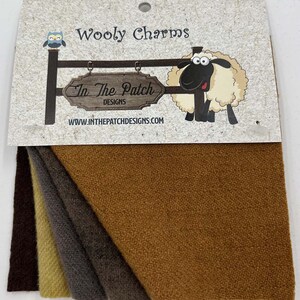 May include: A pack of four wool fabric squares in brown, tan, dark brown, and light brown. The fabric is textured and has a herringbone pattern. The pack is labeled "Wooly Charms" and "In The Patch Designs".