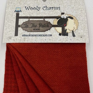 May include: Wooly Charms fabric scraps in a deep red color. The fabric is folded and displayed on a white background. The packaging includes a cartoon sheep and the text "In The Patch Designs" and "www.inthepatchdesigns.com".
