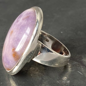 May include: A silver ring with a large oval-shaped purple and white gemstone set in a bezel setting.