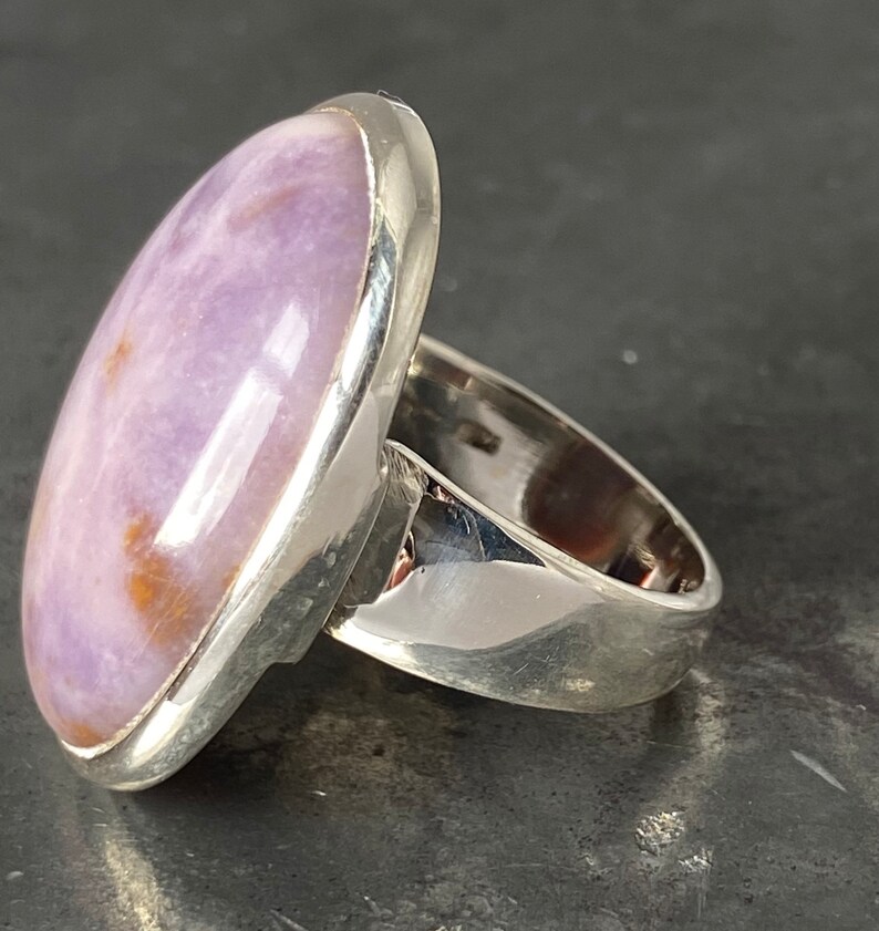 May include: A silver ring with a large oval-shaped purple and white gemstone set in a bezel setting.