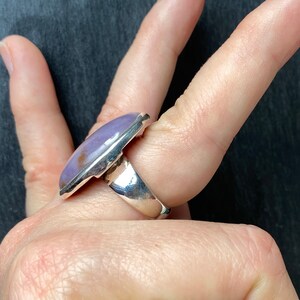 May include: A silver ring with a large, oval-shaped purple gemstone set in a bezel setting.