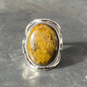 May include: A silver ring with an oval-shaped tiger's eye gemstone. The ring has a unique design with a twisted band.