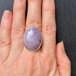May include: A silver ring with a large oval-shaped purple gemstone. The ring is on a person's finger.