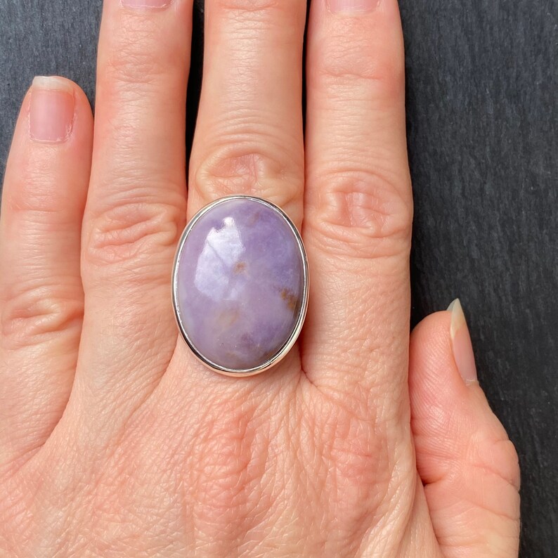 May include: A silver ring with a large oval-shaped purple gemstone. The ring is on a person's finger.