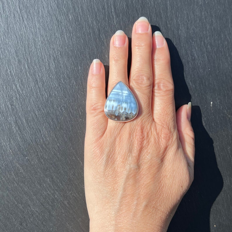 May include: A silver ring with a large, triangular, white and gray gemstone. The ring is on a person's finger.