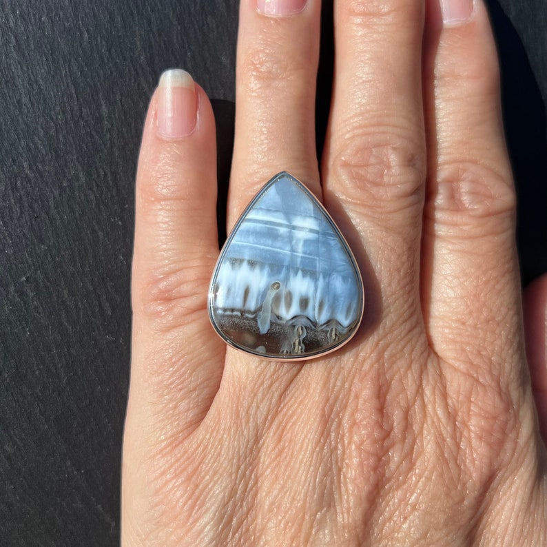 May include: A silver ring with a teardrop-shaped blue and white agate stone.