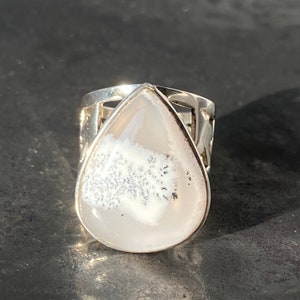 Op de afbeelding: Een zilveren ring met een traanvormige witte agaat-steen. De steen heeft een dendritisch patroon in grijs en zwart.