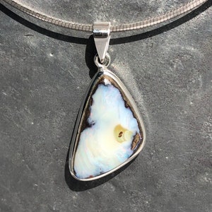 Könnte beinhalten: Eine silberne Kettenkette mit einem Anhänger mit einem weißen Opal-Stein mit schwarzen und braunen Akzenten.