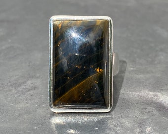 May include: A silver ring with a rectangular, dark brown tiger's eye gemstone.