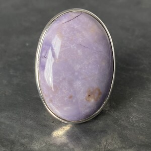 May include: A silver ring with a large oval-shaped purple gemstone. The gemstone has a marbled pattern and a shiny finish.
