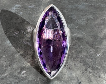 May include: A silver ring with a large, faceted, marquise-shaped amethyst gemstone.