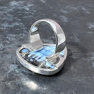 May include: A silver ring with a blue and black iridescent gemstone set in a triangular shape.