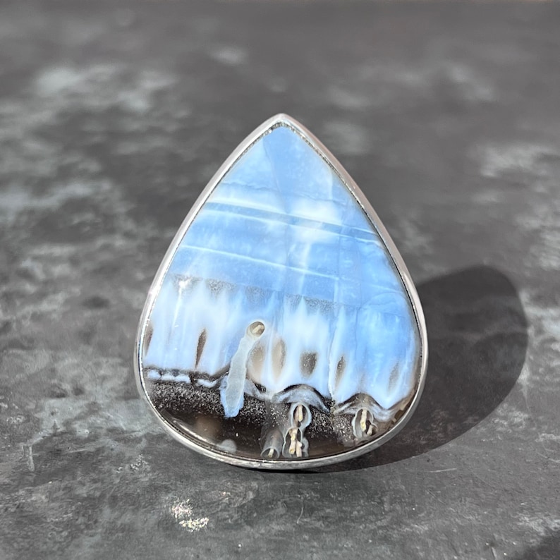 May include: A silver ring with a blue and white opal stone in a teardrop shape.