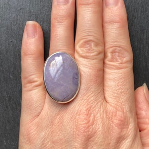 May include: A silver ring with a large oval-shaped purple gemstone. The ring is on a person's finger.