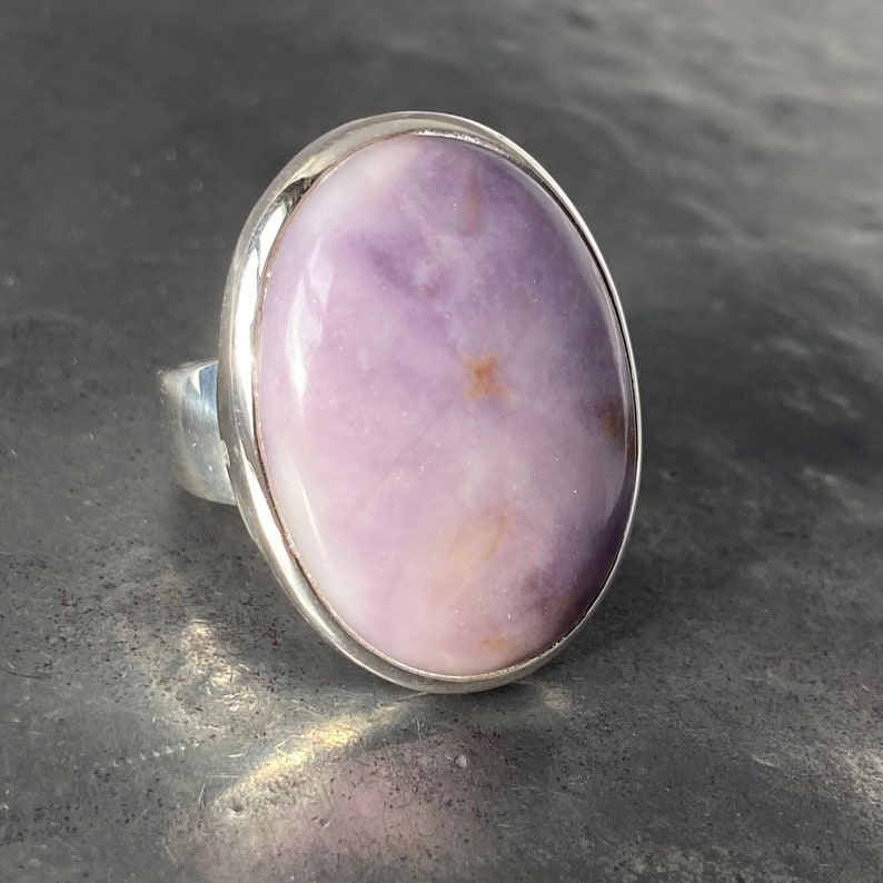 May include: A silver ring with a large oval-shaped purple and white gemstone.