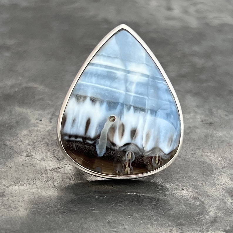 May include: A teardrop-shaped ring with a silver band and a blue and white agate stone.