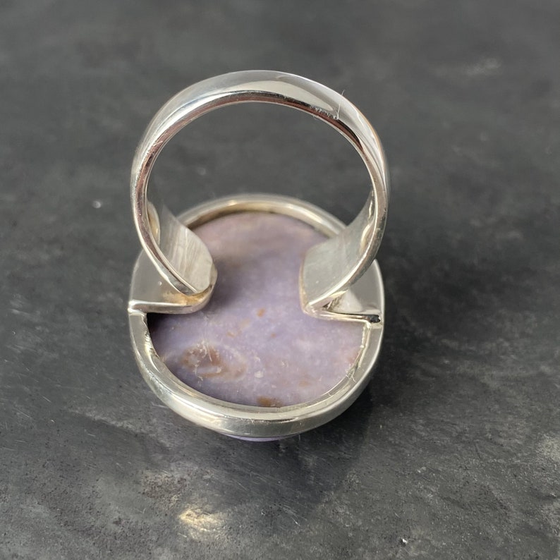 May include: A silver ring with a purple stone set in the center. The ring is oval shaped and has a smooth, polished finish.
