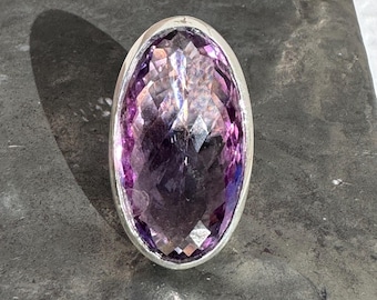 May include: A silver ring with a large, faceted, oval amethyst gemstone.