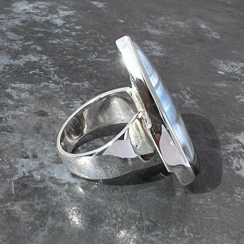 May include: A silver ring with a large, rectangular, blue and white gemstone. The ring is set in a simple, modern style.