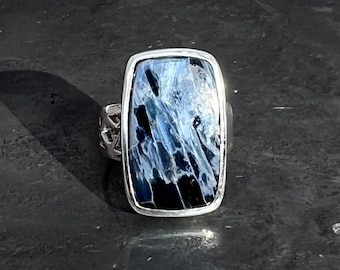 May include: A silver ring with a rectangular blue and black gemstone. The gemstone has a unique pattern of white and blue streaks.