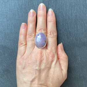 May include: A silver ring with a large, oval-shaped, lavender gemstone. The gemstone has a light purple hue with white and brown inclusions.
