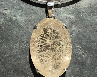 May include: A silver chain necklace with a large oval-shaped pendant featuring a clear quartz crystal with a unique, intricate pattern of inclusions. The crystal is set in a silver bezel.