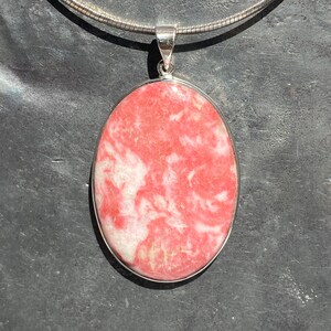 Peut inclure: Un pendentif en argent avec une pierre précieuse ovale rose et blanche. Le pendentif est sur une chaîne en argent.