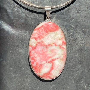 Peut inclure: Un pendentif en argent avec une pierre précieuse ovale rose et blanche. La pierre précieuse présente un motif tourbillonnant de rose et de blanc.