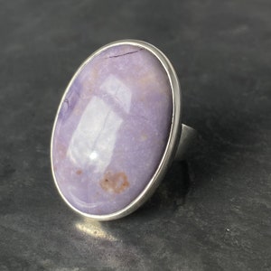 May include: A silver ring with a large oval-shaped purple gemstone set in a bezel setting.