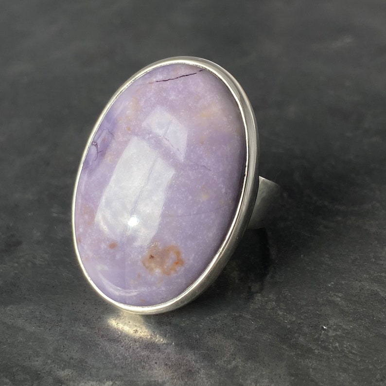 May include: A silver ring with a large oval-shaped purple gemstone set in a bezel setting.