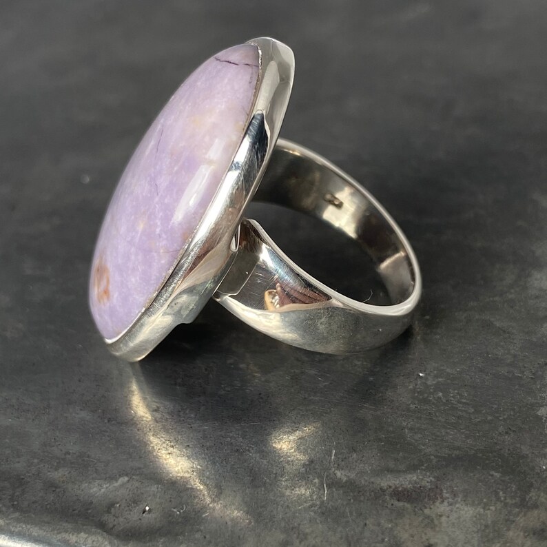 May include: A silver ring with a large oval-shaped lavender gemstone set in a bezel setting.