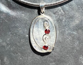 May include: A silver necklace with a white oval pendant featuring a silver swirl design and three red gemstones.