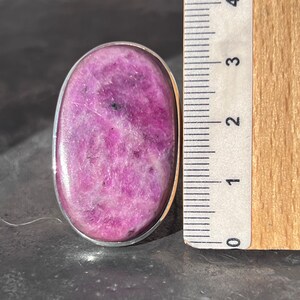 Peut inclure: Une bague ovale avec une pierre pr&eacute;cieuse rose vif polie, sertie dans un m&eacute;tal argent&eacute;. La pierre a un aspect mouchet&eacute; avec des taches plus fonc&eacute;es. La bague mesure environ 3,8 cm de long.