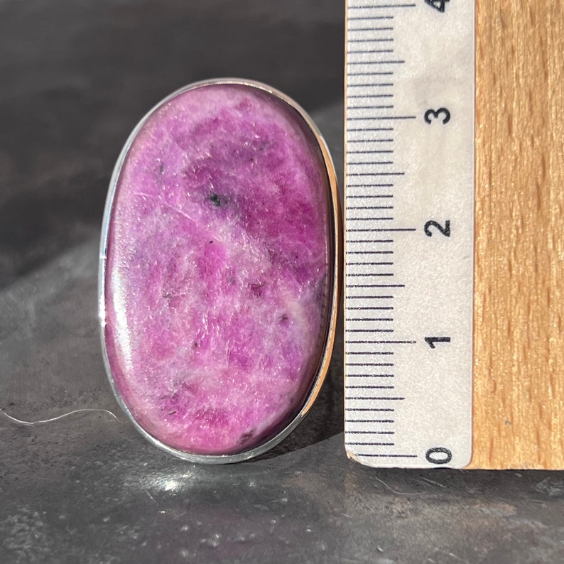 Peut inclure: Une bague ovale avec une pierre pr&eacute;cieuse rose vif polie, sertie dans un m&eacute;tal argent&eacute;. La pierre a un aspect mouchet&eacute; avec des taches plus fonc&eacute;es. La bague mesure environ 3,8 cm de long.