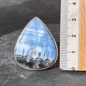 May include: A teardrop-shaped ring with a blue and white opal stone set in silver. The stone has a unique pattern of white and blue swirls.