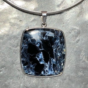 Op de afbeelding: Een zilveren ketting met een vierkante hanger met een zwarte en blauwe tijgeroog edelsteen.