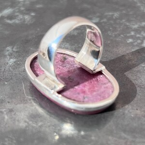 Peut inclure: Une bague en argent avec une pierre pr&eacute;cieuse rose ovale. La pierre pr&eacute;cieuse a un aspect textur&eacute; et est sertie dans une monture en argent poli. Le design de la bague est simple, mettant l'accent sur la couleur et la forme de la pierre.