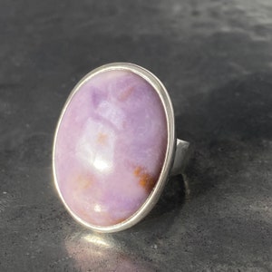 May include: A silver ring with a large oval purple and white gemstone set in the center.