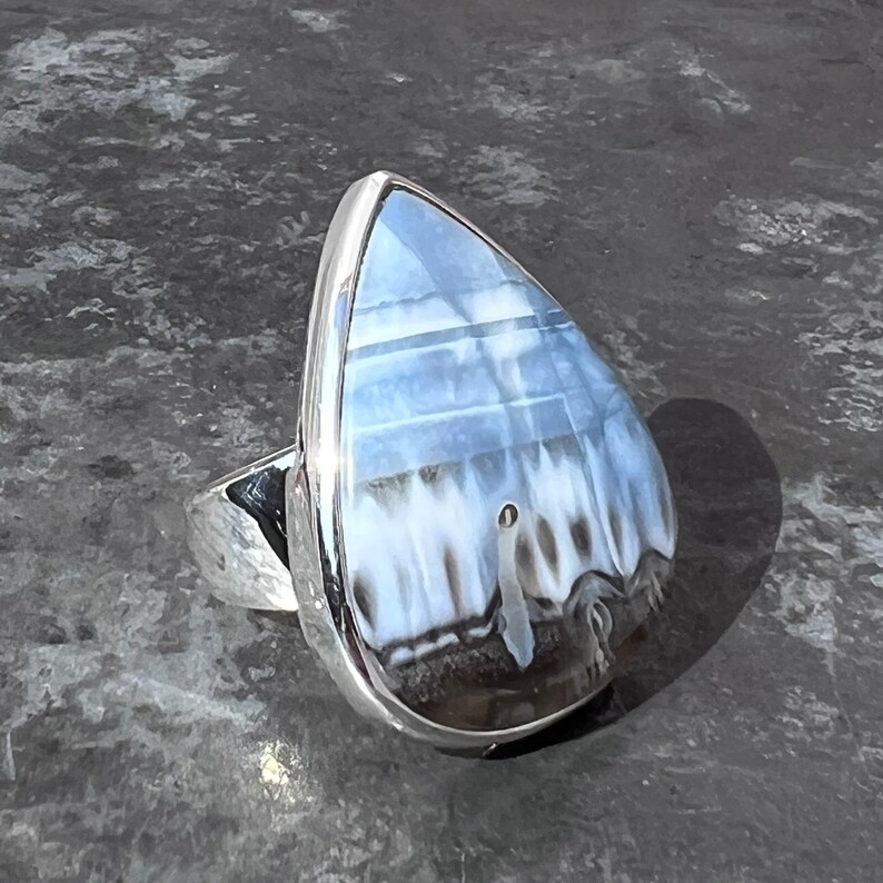 May include: A silver ring with a teardrop-shaped blue and white agate stone.