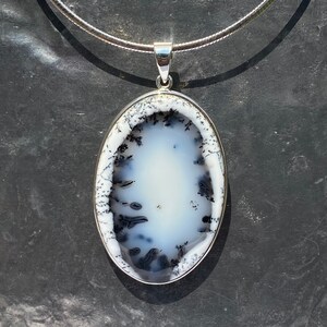 Op de afbeelding: Een zilveren ketting met een ovale hanger met een witte dendritische agaat steen met zwarte dendrieten.
