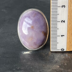 May include: A silver ring with a large oval-shaped purple and brown gemstone. The ring is next to a ruler, showing the stone is approximately 1 inch in diameter.