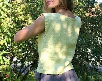 May include: A light yellow sleeveless linen top with a scoop neck. The top is made of a lightweight fabric and has a relaxed fit.