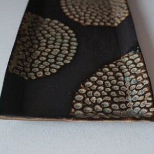 May include: A black rectangular ceramic serving tray with a decorative pattern of brown and white circles with blue accents.