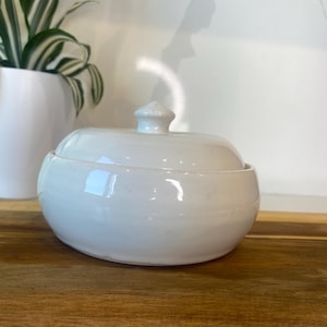 May include: White ceramic bowl with a lid. The bowl is round and has a smooth, glossy finish.
