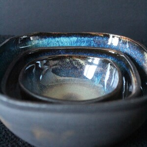 Puede incluir: Un juego de tres cuencos encajables con un esmalte azul oscuro y negro. Los cuencos est&aacute;n hechos de cer&aacute;mica y tienen una forma ligeramente irregular.